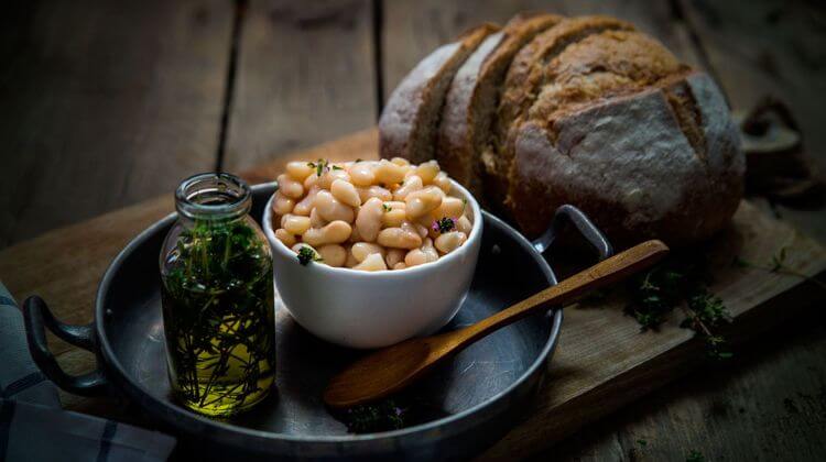 Bol de haricots tarbais cuisinés à la graisse de canard dans un ramequin blanc posé à coté d'un flacon d'huile d'olive et d'une miche de pain